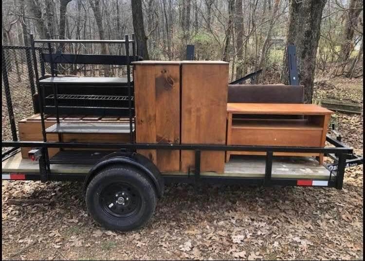 Utility trailer loaded with a wooden dresser, cabinet and shelving unit removed from a home